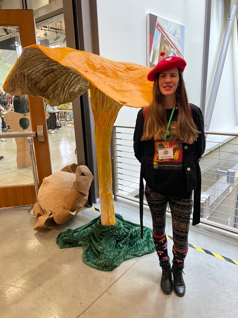 Cassandra Beaumont beside a large mushroom sculpture at a mycology gathering